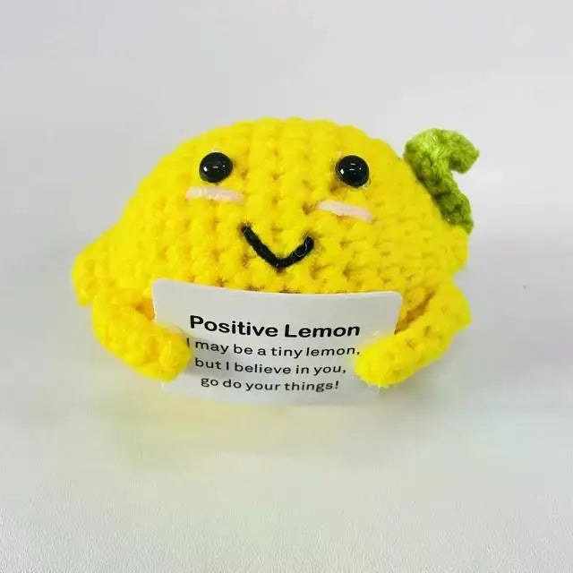 A yellow plush toy resembling a lemon with a sign holding an inspirational message, placed on a white surface